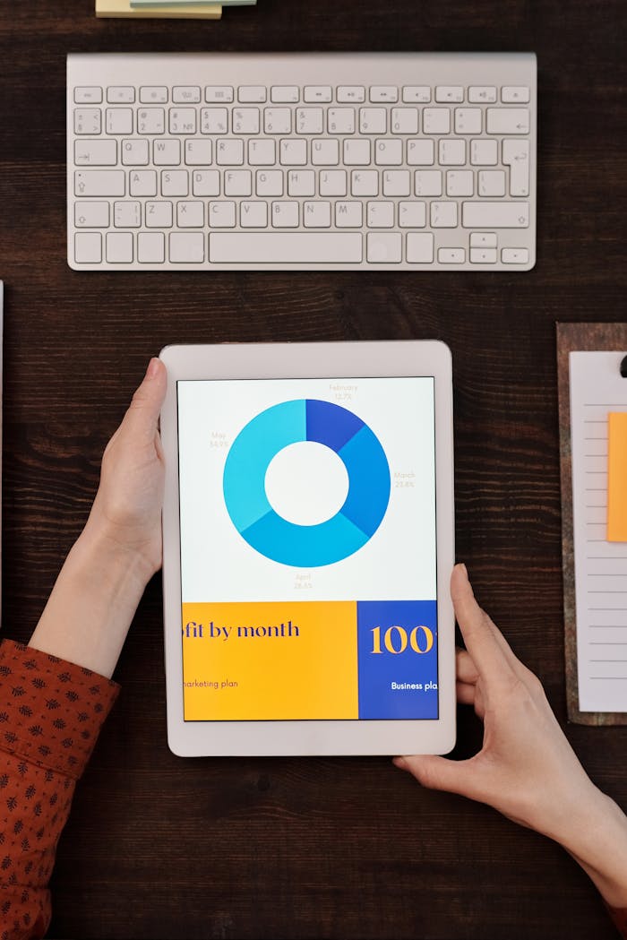 about-us-02 A person holds a tablet showing a business graph next to a keyboard on a wooden desk.